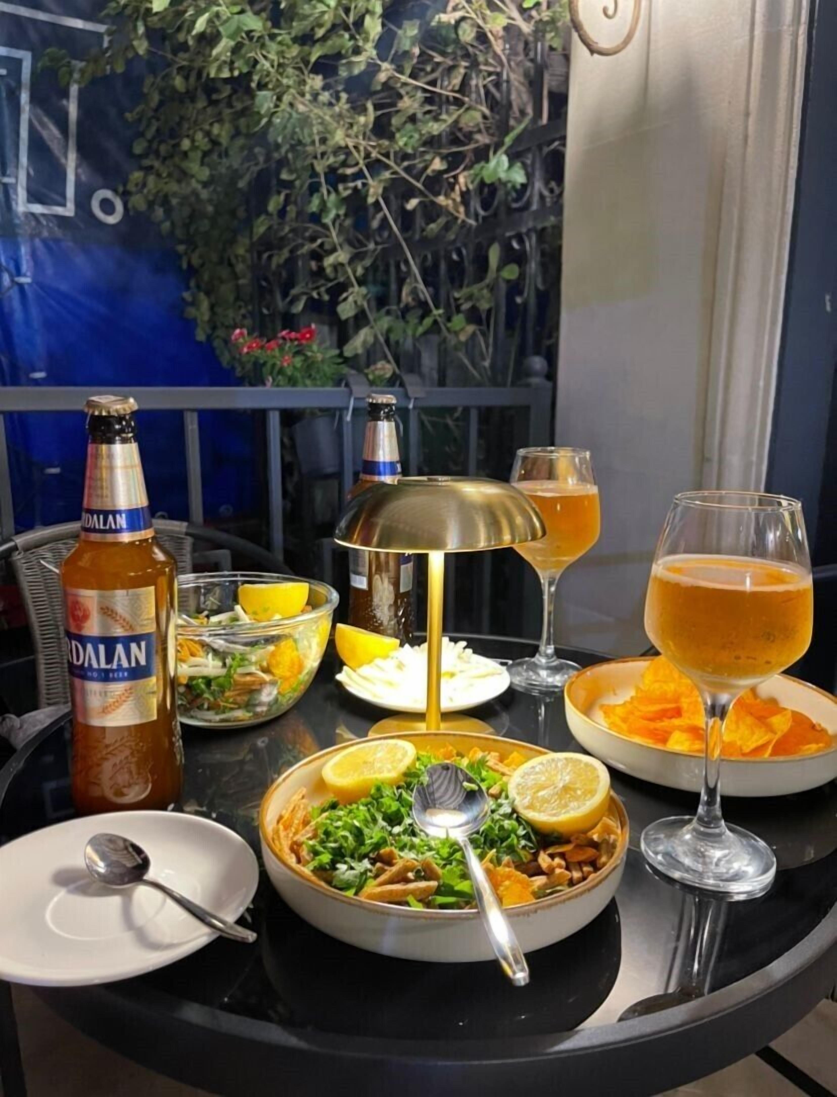 Une table dressée pour le dîner, avec une bouteille de bière, une salade, un verre de bière et un cocktail.