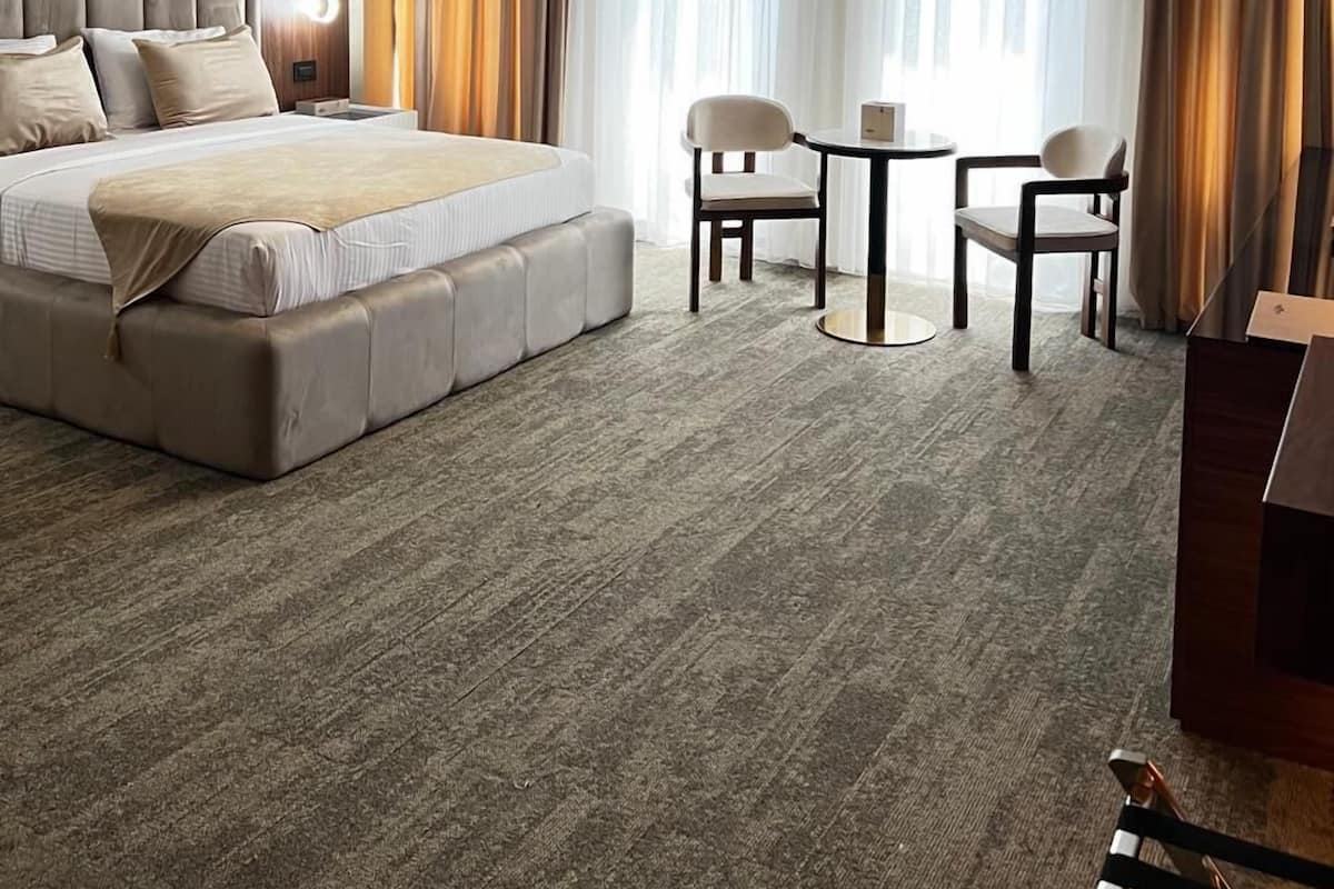 Ein modernes Hotelzimmer mit einem großen Bett, einem kleinen Tisch, zwei Stühlen und einer Deckenleuchte.