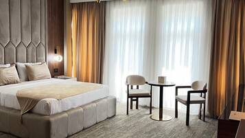 A modern hotel room with a large bed, a small table, two chairs, and a ceiling-mounted light fixture.