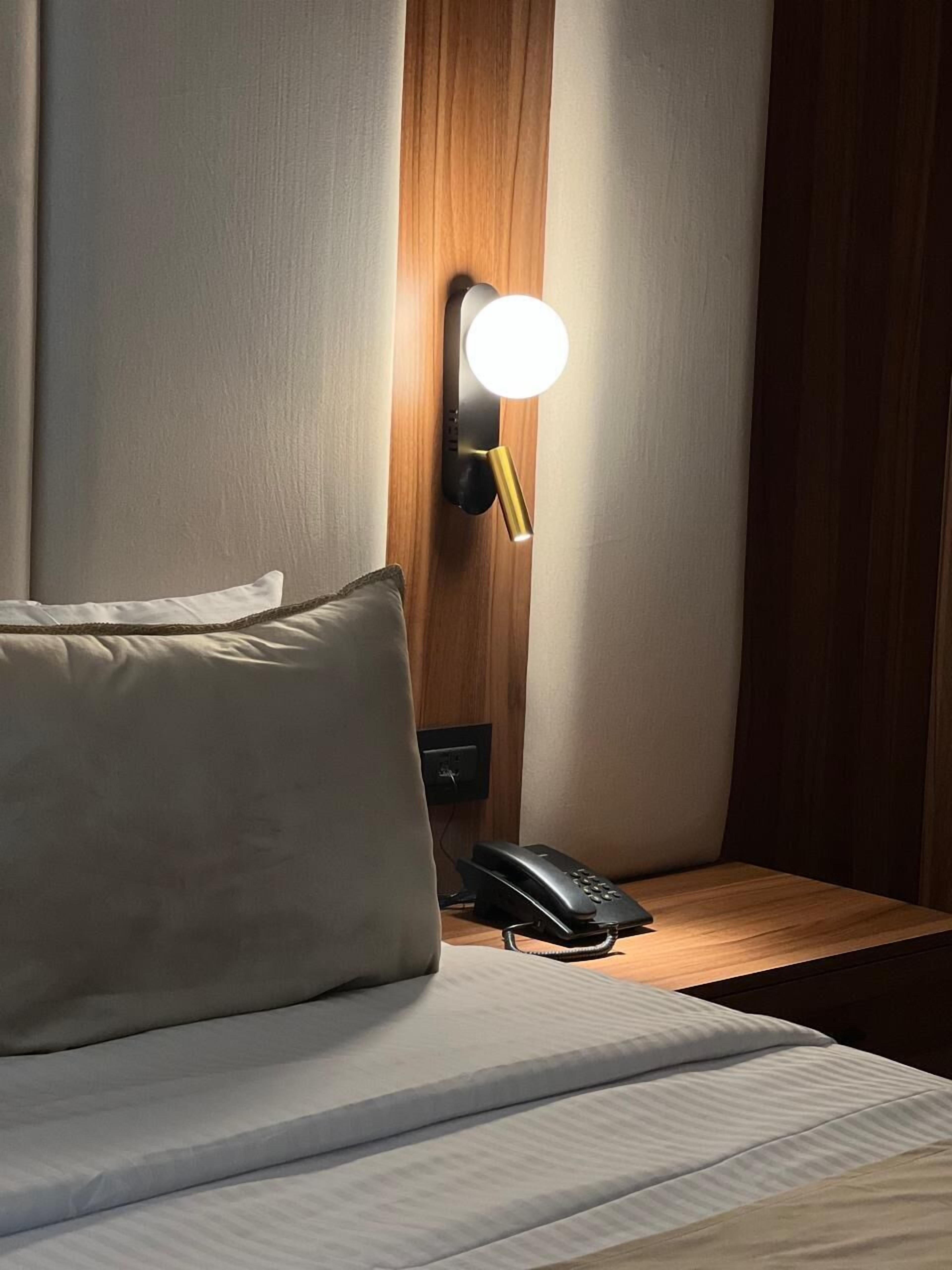 Habitación de hotel con una cama, una lámpara de noche, un teléfono y una lámpara de pared.