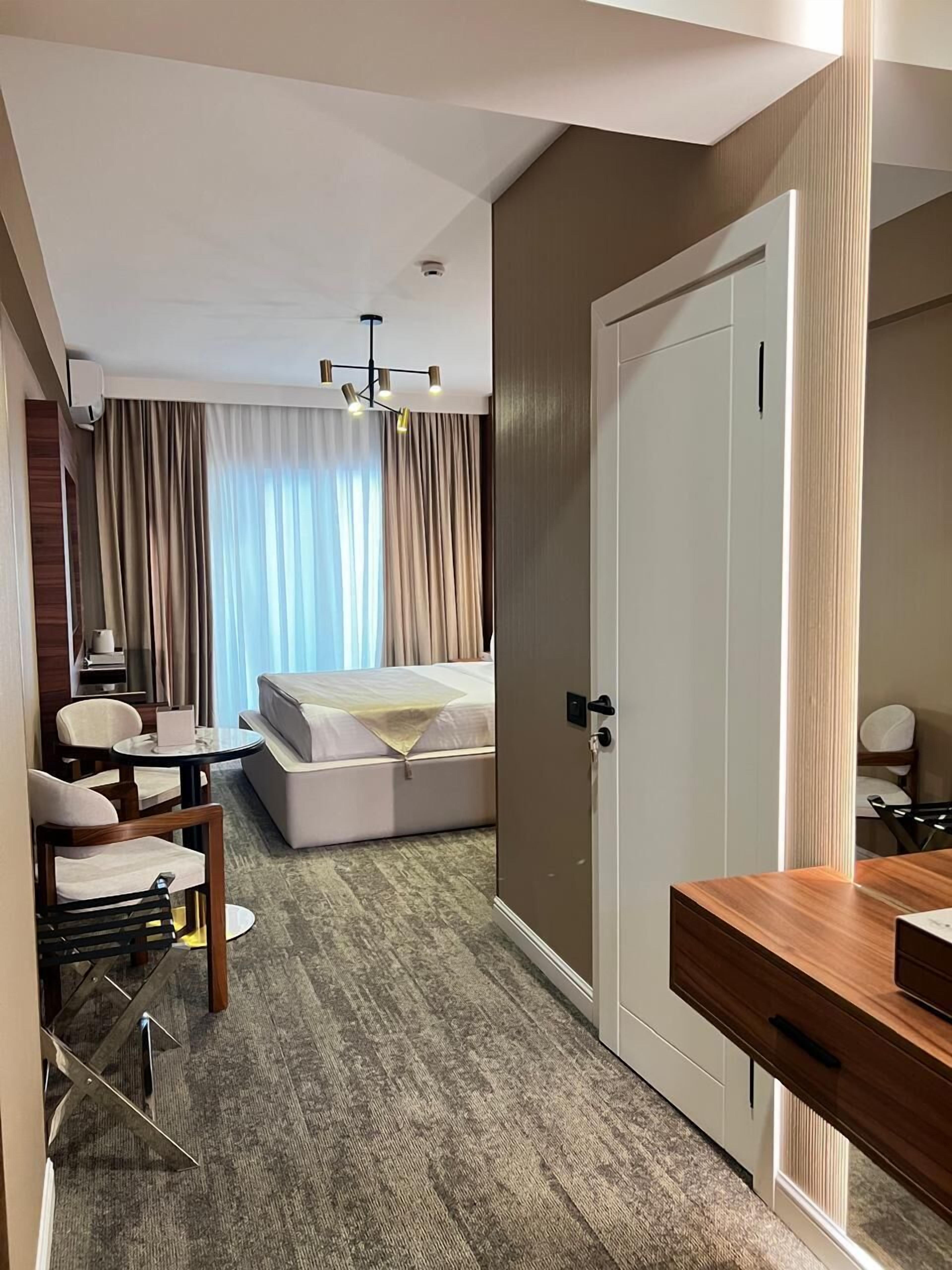 Une chambre d’hôtel avec un lit, un bureau, une chaise, un miroir et une porte.