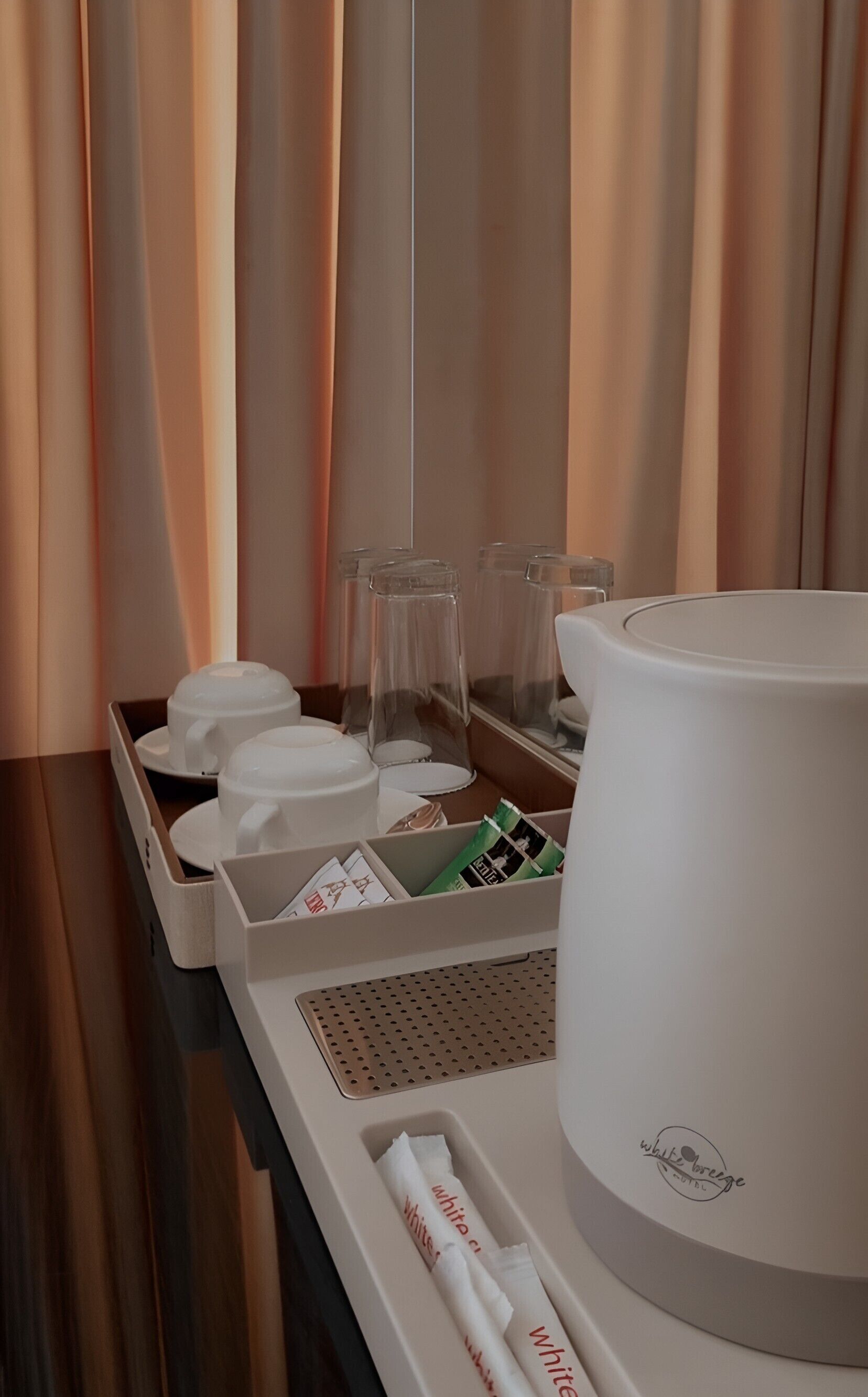 A hotel room with a coffee machine, tea set, and a tray with glasses and napkins.