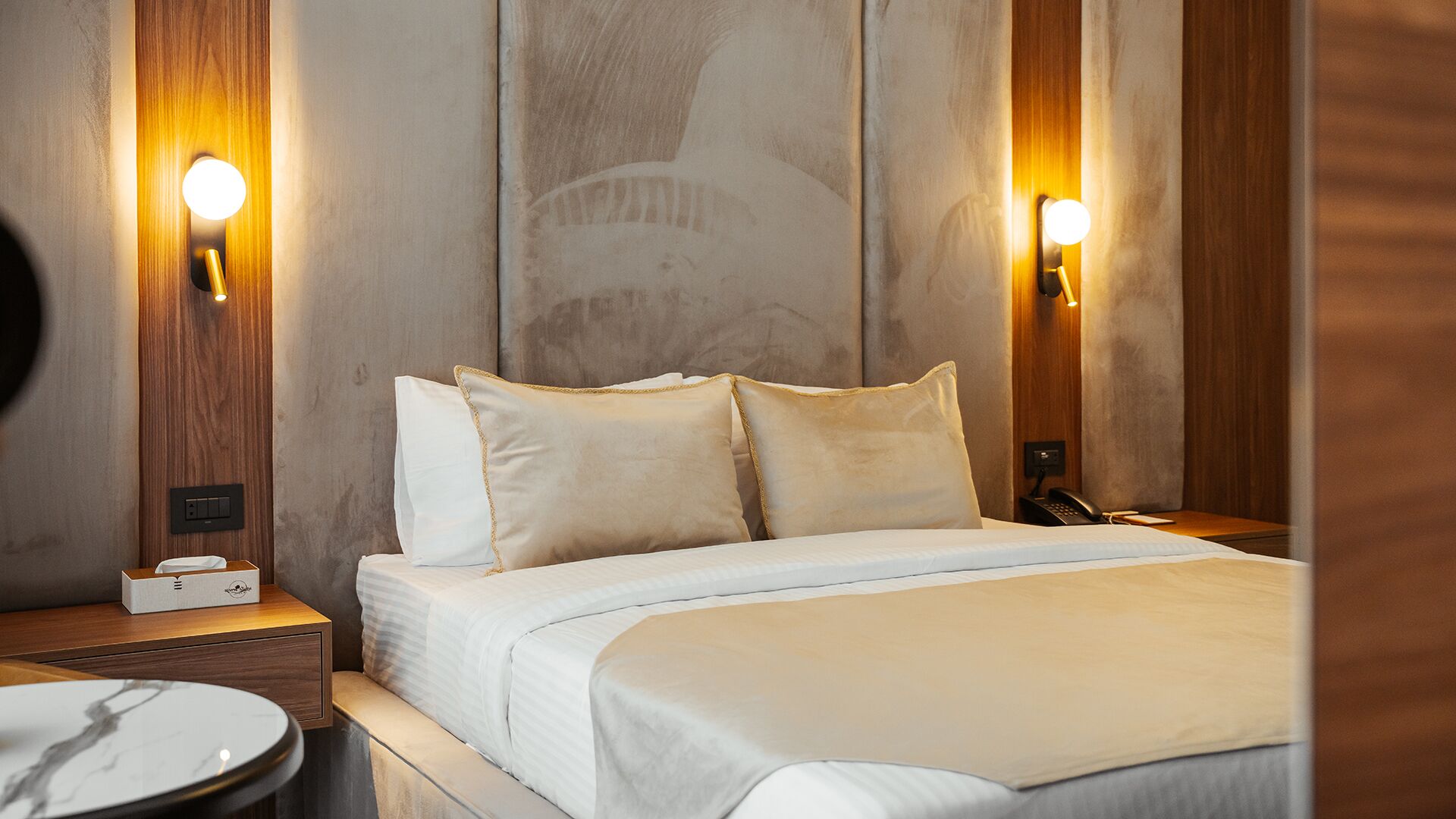 A hotel room with a bed, bedside tables, and wall-mounted lamps.
