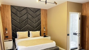 Ein modernes Hotelzimmer mit einem großen Bett, einem Kopfteil mit geometrischem Muster, Nachttischlampen und Blick ins Badezimmer durch eine geöffnete Tür.