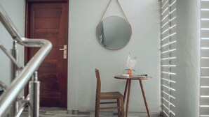 A hallway with a wooden door, a round mirror on the wall, a small table with a chair, and a tiled floor. - 4040 Accomodation (Matola)