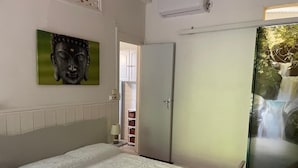 Ein Schlafzimmer mit Bett, Kleiderschrank, Buddha-Statue an der Wand und einer Glasdoppeltür mit Blick auf einen Wasserfall.