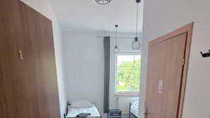 A room with a bed, a small table, a window with curtains, and a door. - Średzka Korona (Środa Śląska)