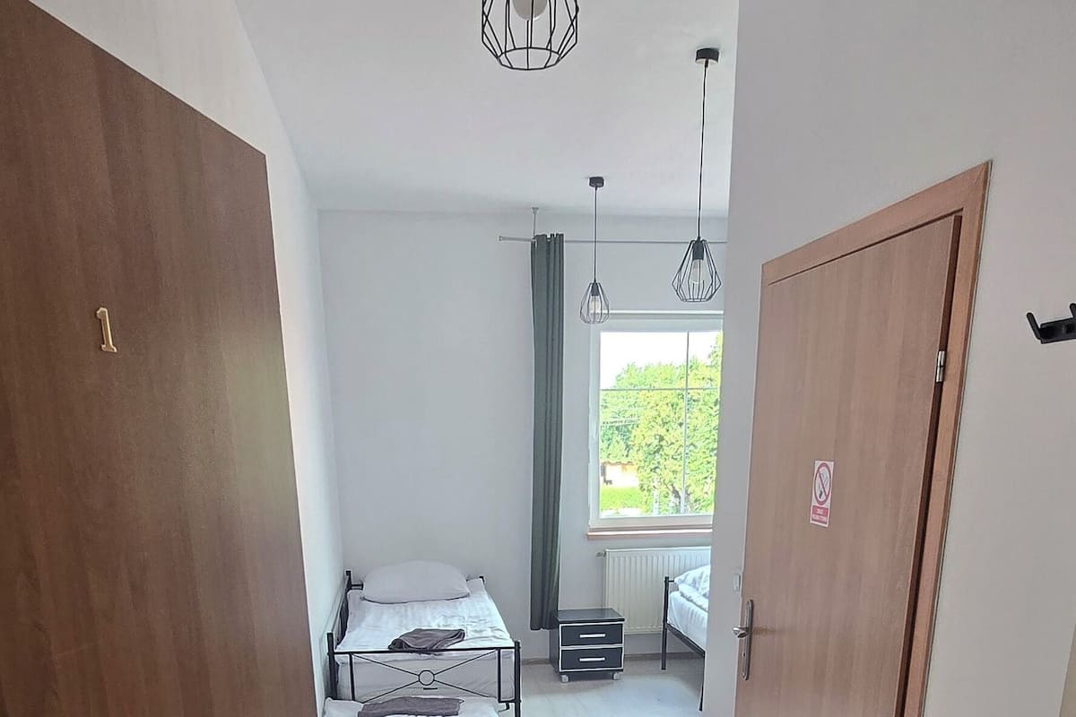 Una habitación con cama, una mesita, una ventana con cortinas y una puerta.