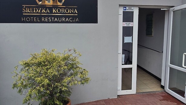 A hotel entrance with a sign reading "SREDZKA KORONA HOTEL RESTAURACJA" and a potted plant in front. - Średzka Korona (Środa Śląska)
