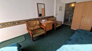 Habitación de hotel con cama, dos sillones, una mesita de madera, un espejo, armario y baño visible a través de una puerta abierta.