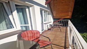 Un balcón con piso de madera, una mesa de vidrio y una silla a rayas rojas.