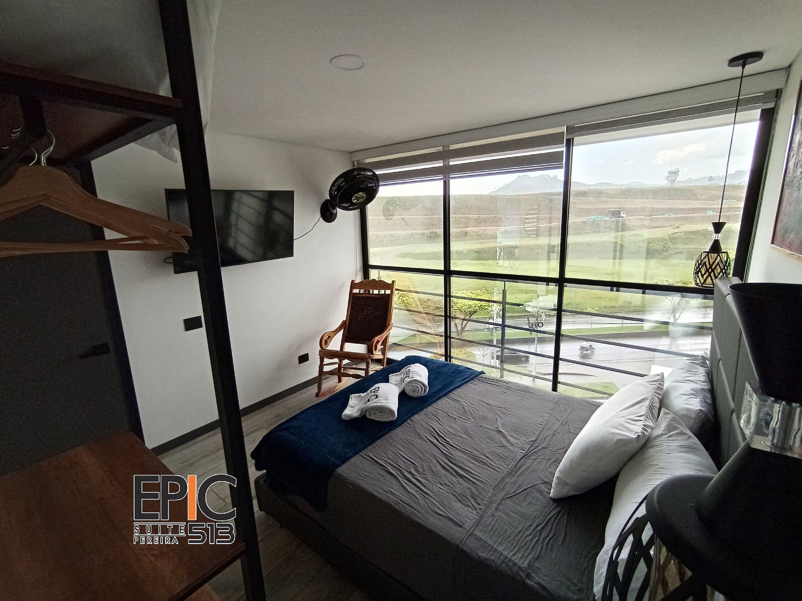 A modern hotel room with a large bed, a chair, a TV, and a view of the landscape.