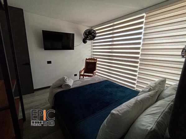 Una habitación de hotel moderna con una cama, una silla, un televisor montado en la pared y una ventana con persianas.