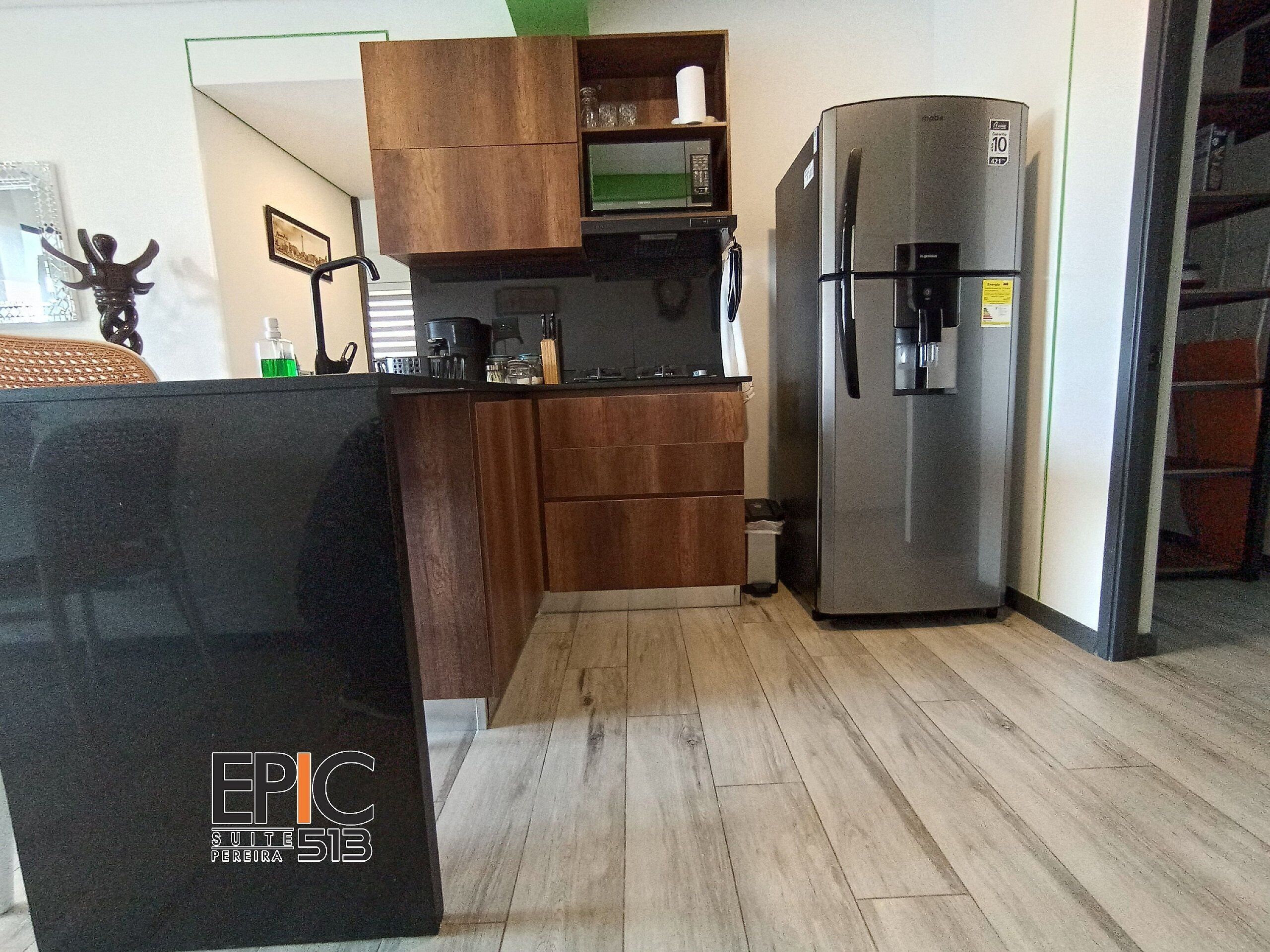 Una cocina compacta con armarios de madera, un refrigerador de acero inoxidable y una encimera negra.