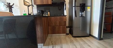 Una cocina compacta con armarios de madera, un refrigerador de acero inoxidable y una encimera negra.