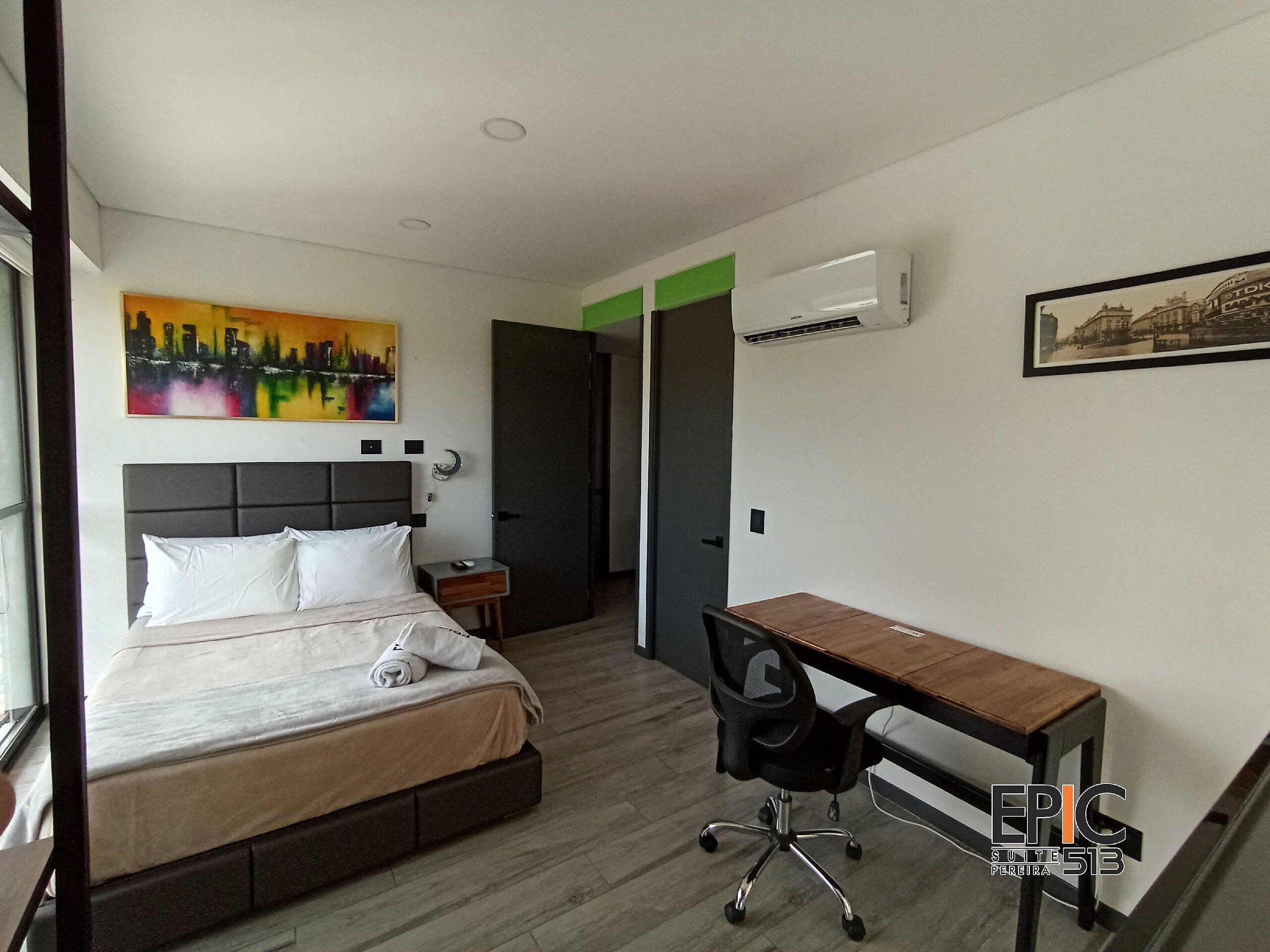 A hotel room with a bed, desk, chair, and artwork on the walls.