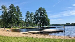 Un parque junto al lago con una playa de arena, un muelle de madera y una zona cubierta de césped.