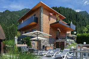 Ein modernes, zweistöckiges Haus mit Balkon, Außenbereich und Blick auf einen bewaldeten Berg.