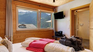 A room with a bed, a TV mounted on the wall, and a window with a mountain view.
