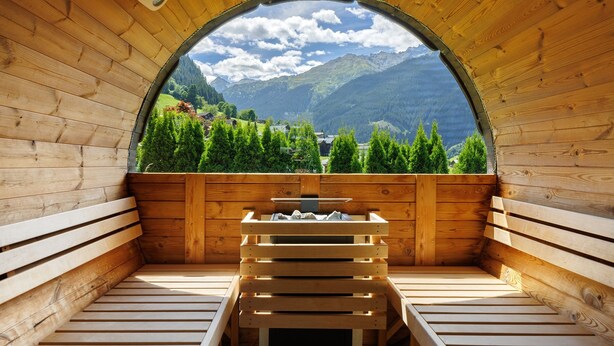 A sauna with a wooden interior, a bench, and a view of mountains and greenery.