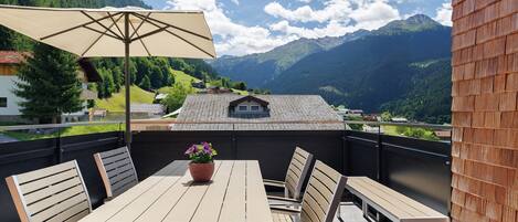 Eine Terrasse mit Tisch und Stühlen, einem Blumentopf und Blick auf Berge.