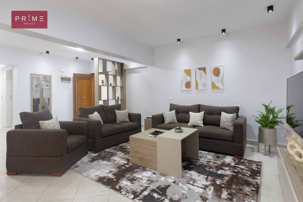 A modern living room with two sofas, a coffee table, and a rug. There are wall art pieces and a plant on the wall.