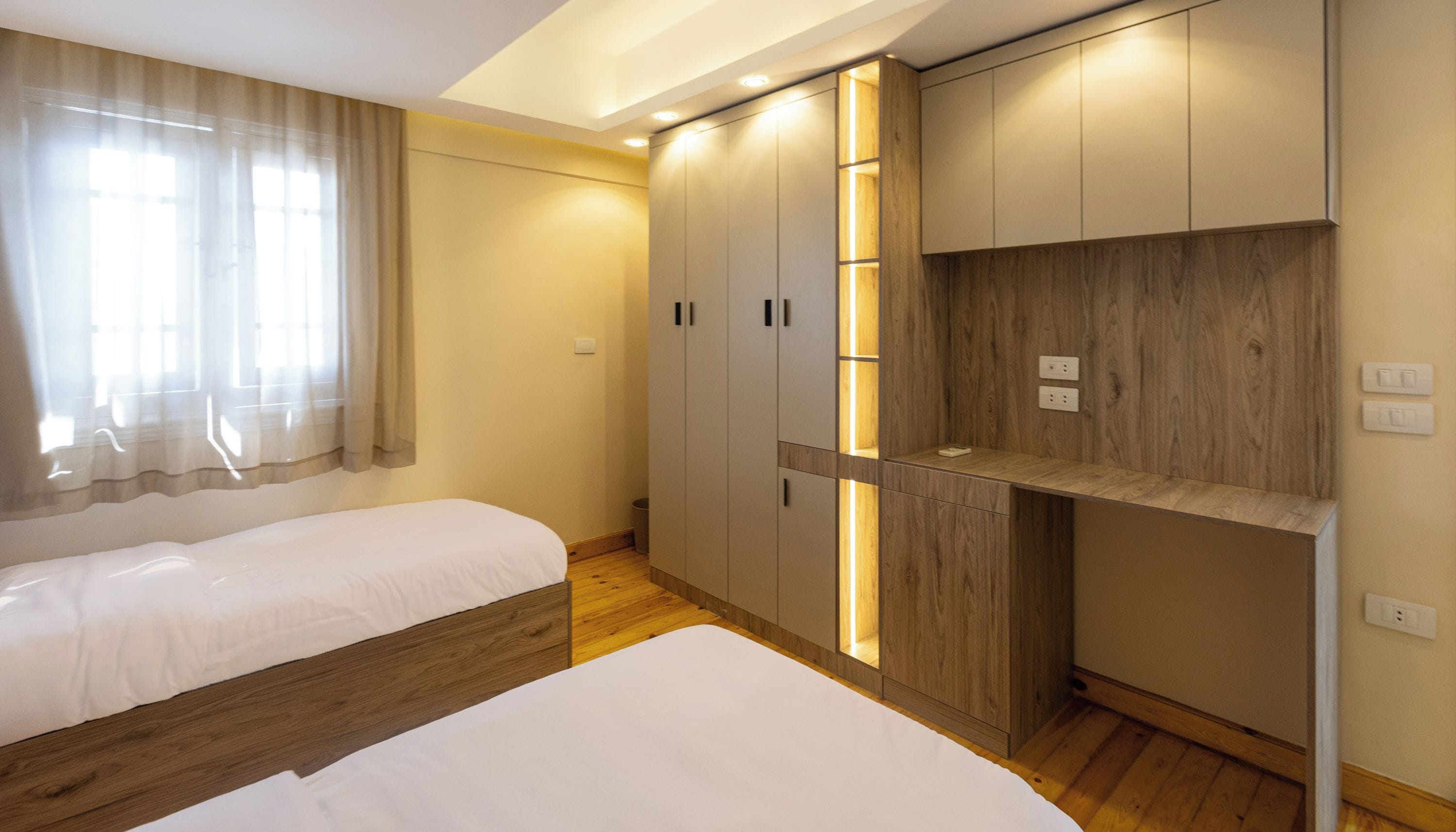 A modern hotel room with two beds, built-in wardrobes, and a wooden floor.
