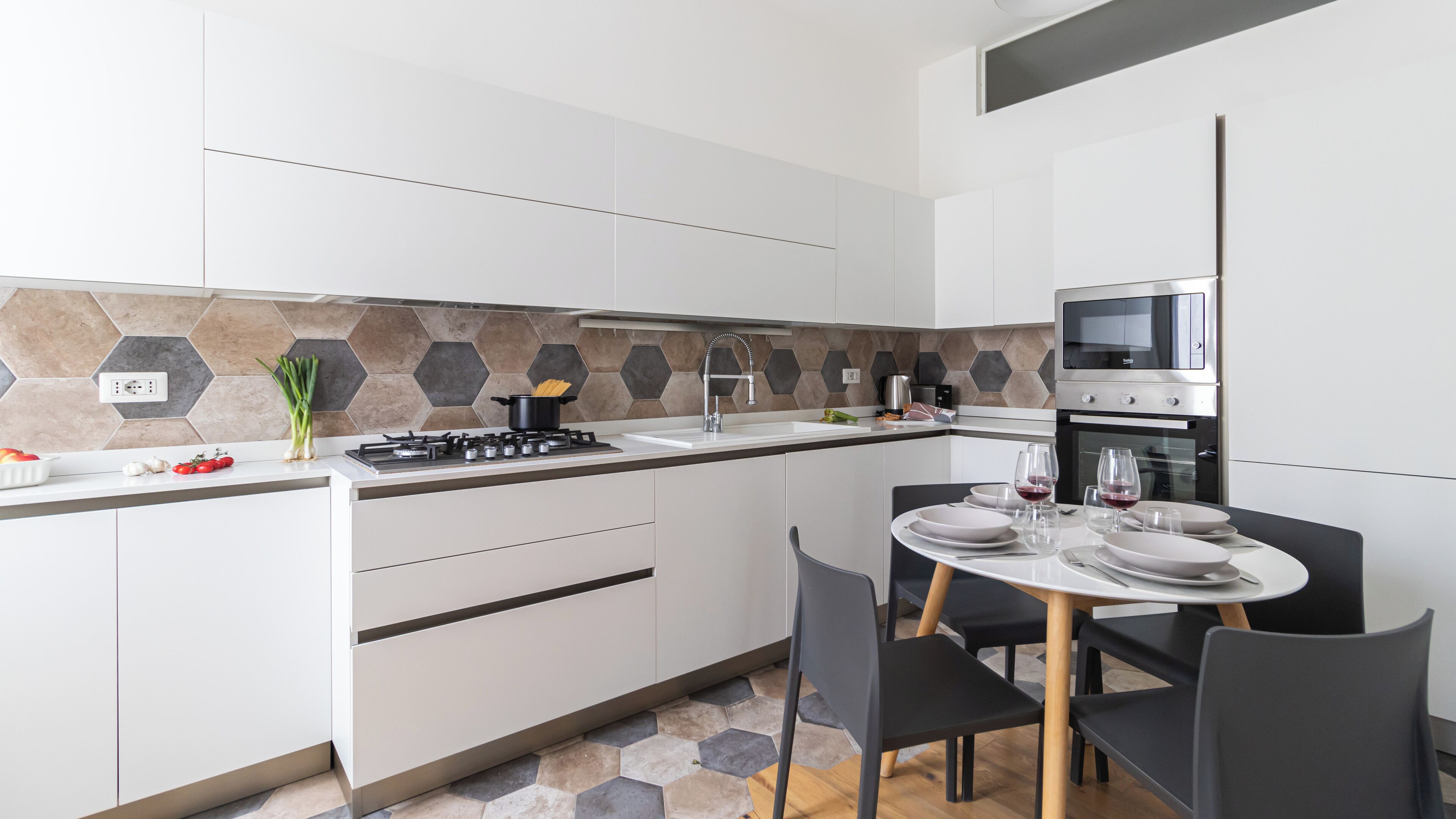 Een moderne keuken met witte kasten, een gasfornuis en een magnetron. Er is een zithoek met een tafel gedekt voor twee personen.