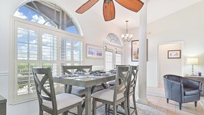 A dining area with a large table, four chairs, a ceiling fan, and large windows. - Waterfront Executive 3-bedroom property, private location and peaceful! (Cape Coral)