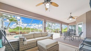 A spacious patio area with a large sofa, ottoman, and dining table, featuring a view of a pool and greenery. - Waterfront Executive 3-bedroom property, private location and peaceful! (Cape Coral)