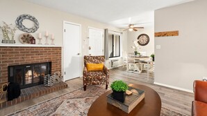 Un salon avec une cheminée, un fauteuil à motifs, une table basse et, au fond, un coin repas.