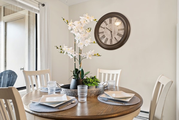 Una mesa de comedor con sillas, un reloj y un jarrón de flores.