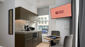 Eine kompakte Küche mit modernen Geräten, ein Essbereich mit einem kleinen Tisch und Stühlen sowie ein Fernseher, der „GUEST READY“ anzeigt.