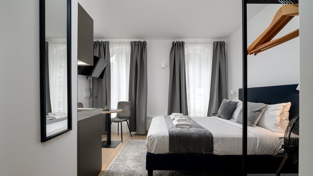 Ein modernes Hotelzimmer mit Bett, Nachttisch, Sessel und Schreibtisch.