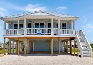 Una casa sulla spiaggia su due piani con un portico coperto, un garage e una scala che conduce al piano superiore.