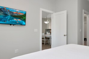 Una camera da letto con un letto grande, una TV a parete che mostra un paesaggio montano e un'apertura che dà su un'area pranzo.