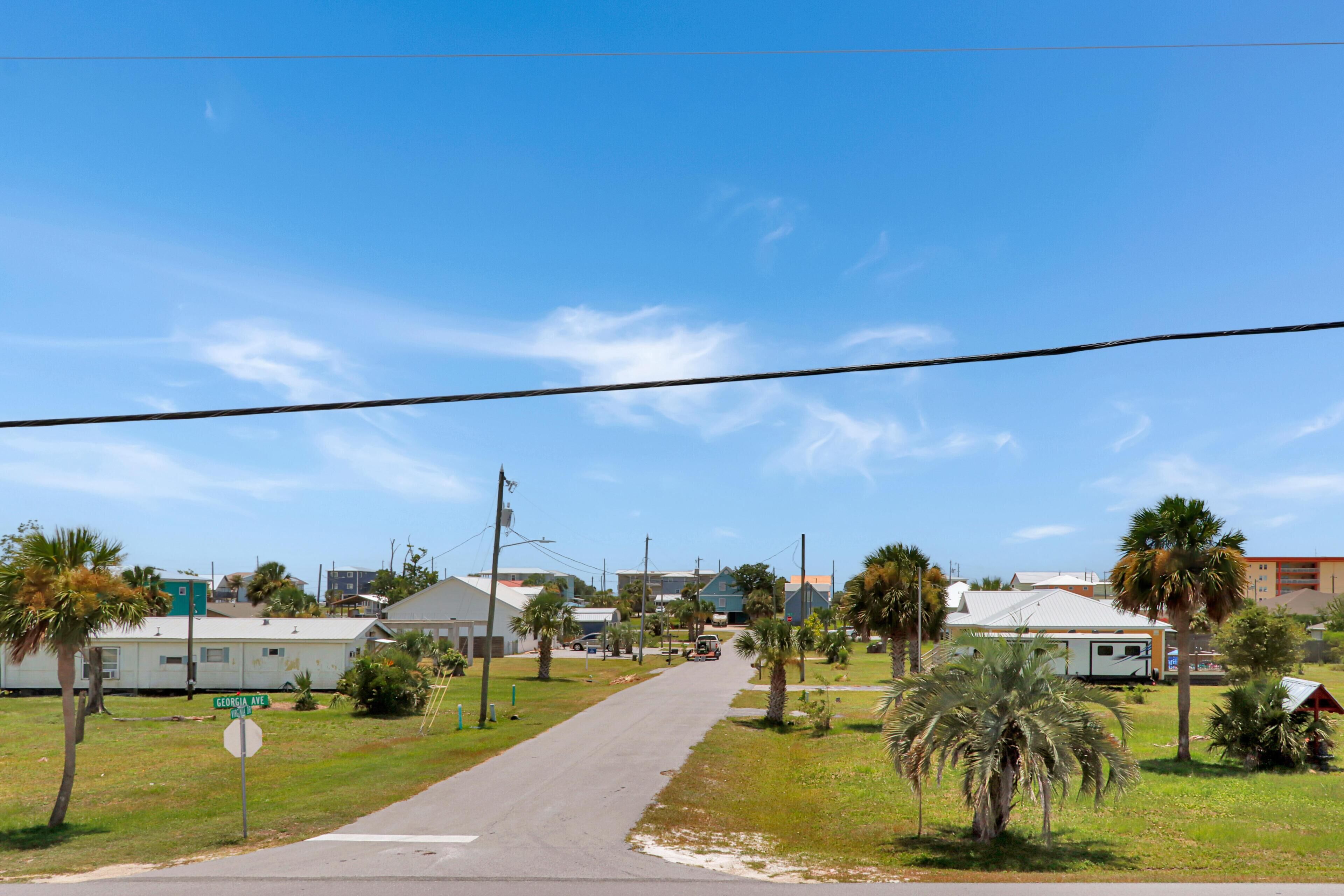 Une rue résidentielle bordée de maisons, un ciel dégagé et des lignes électriques aériennes.
