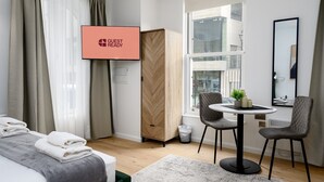 Hotellihuone, jossa on sänky, työpöytä ja kaksi tuolia, seinälle asennettu televisio ja ikkuna, josta on näkymä rakennuksiin.