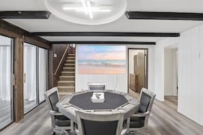 Quarto com uma mesa redonda, quatro cadeiras, vista para a praia, uma escada e uma porta que dá para outro cômodo.