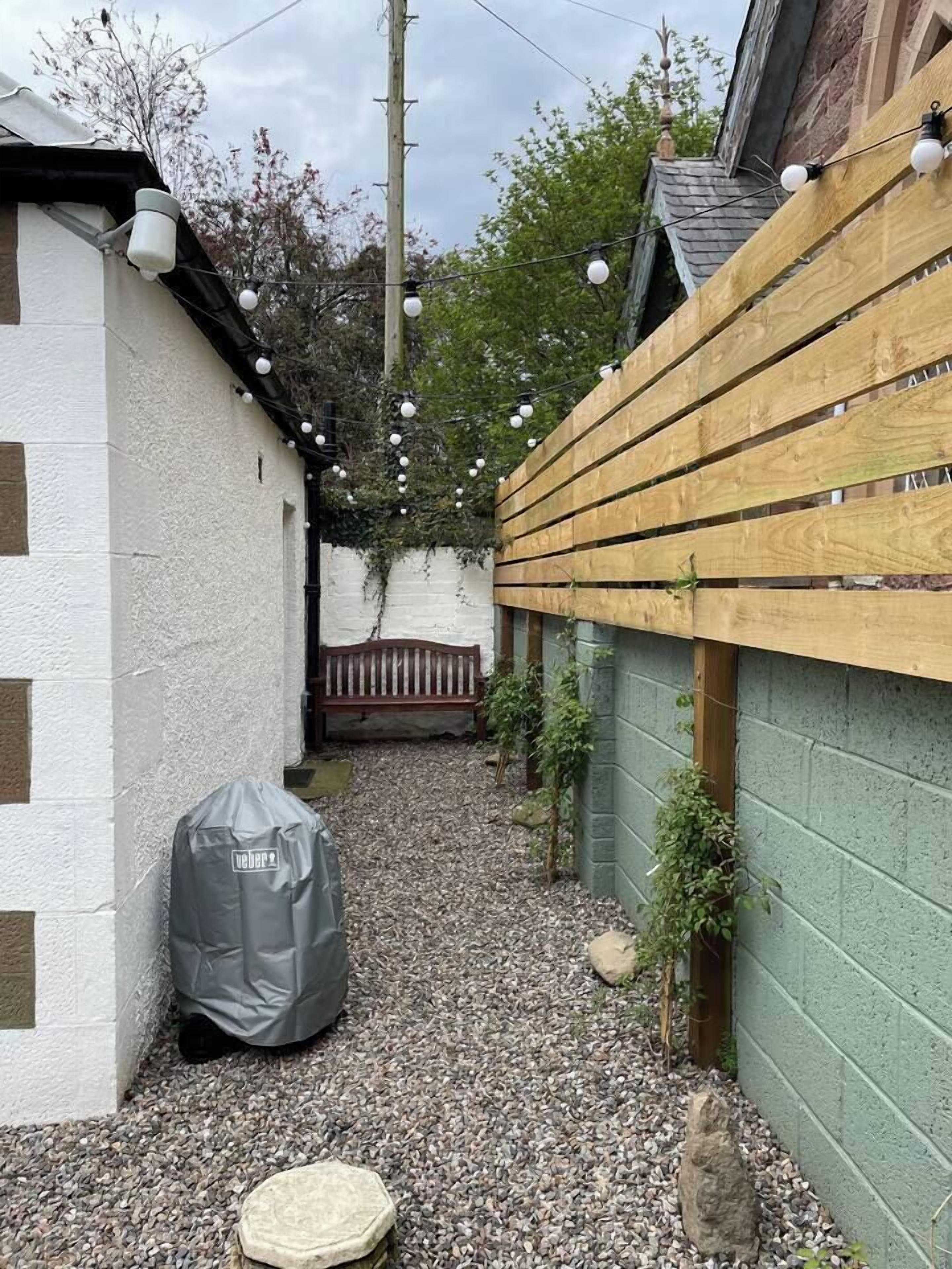 A narrow outdoor space with a gravel path, a wooden fence, and a bench.