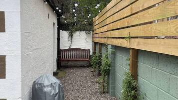 A narrow outdoor space with a gravel path, a wooden fence, and a bench.