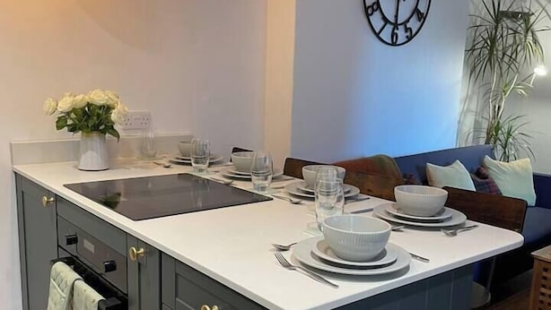 Een moderne keuken met een centraal eiland, grijze kastjes en een wit aanrecht.