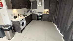 A modern kitchen with dark cabinets, a built-in washing machine, a stove, and a sink. - Charming 3 Bedroom House in West London (London)