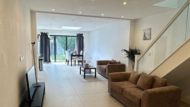 A spacious living area with a sofa set, a coffee table, and a TV on a stand. There is a staircase leading to an upper level. - Charming 3 Bedroom House in West London (London)
