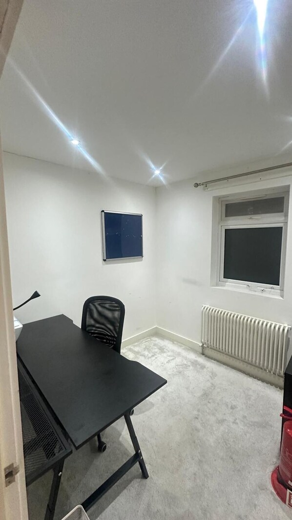 A small, well-lit room with a black table, a single black chair, a white radiator, and a window with a white frame. - Charming 3 Bedroom House in West London (London)