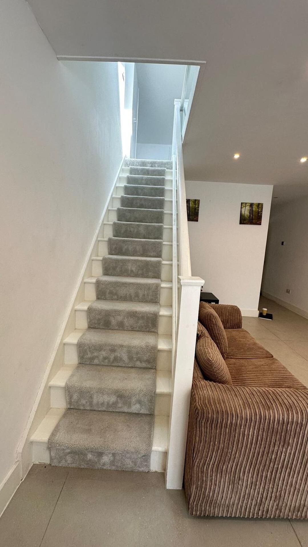 Un escalier dont les marches sont recouvertes de moquette, menant à un palier où se trouve un canapé marron à motifs en relief.