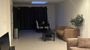 A modern living room with a flat-screen TV, a sofa, a dining table with chairs, and a ceiling light. - Charming 3 Bedroom House in West London (London)