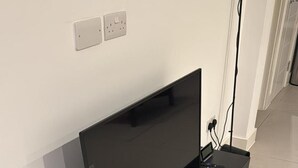 A black TV stand with a flat-screen TV, a remote, and a power cord. - Charming 3 Bedroom House in West London (London)