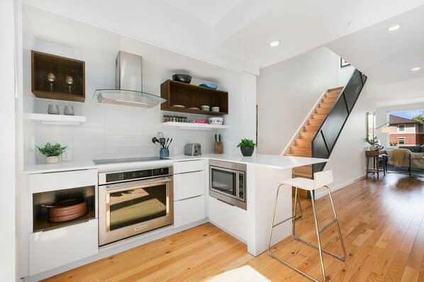 A modern kitchen with white cabinetry, stainless steel appliances, and a wooden staircase. - The Overlook - Luxe Old Town Condo w/ King Suite (Fort Collins)