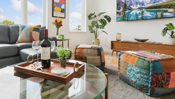 A modern living room with a sofa, coffee table, and a painting of a mountain landscape. - The Overlook - Luxe Old Town Condo w/ King Suite (Fort Collins)